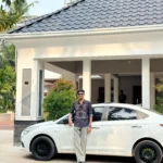 A stylish man stands confidently beside a white car in front of a modern home, exemplifying the top digital marketing strategist in Kannur.